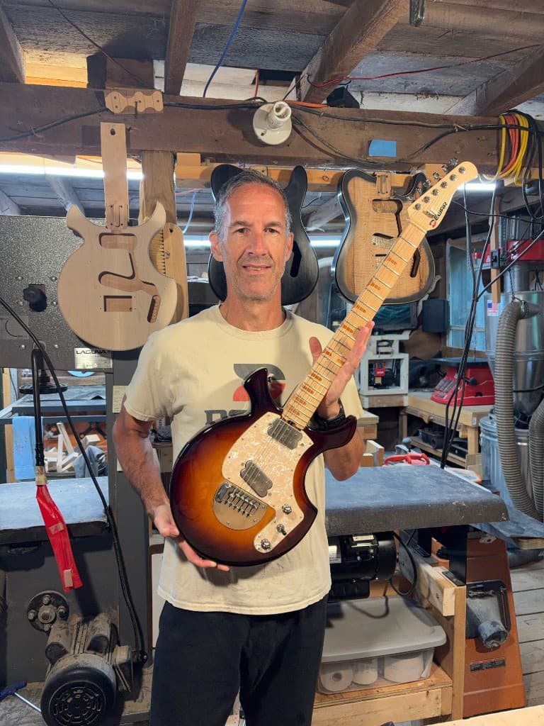 Master luthier Jim Dewar holding a finished guitar in his Holliston workshop